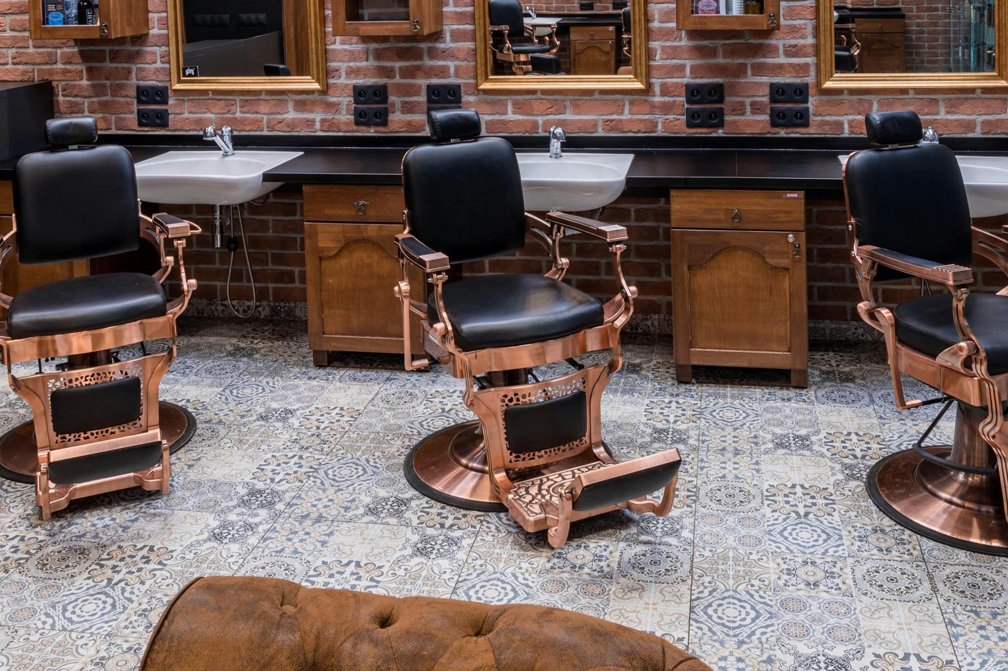 Barbershop interior with vintage chairs, wash basins and gold-framed mirrors on a brick wall